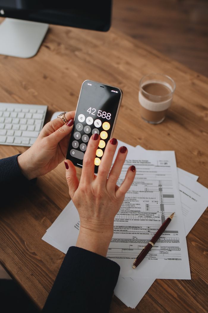 Mastering the First Impression: Your intriguing post title goes here Hands using smartphone calculator over documents on a wooden table, indicating financial calculation or budgeting.